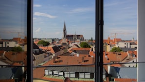 Vista de un paisaje urbano a través de una ventana, con una aguja de iglesia destacada, varios edificios y tejados.