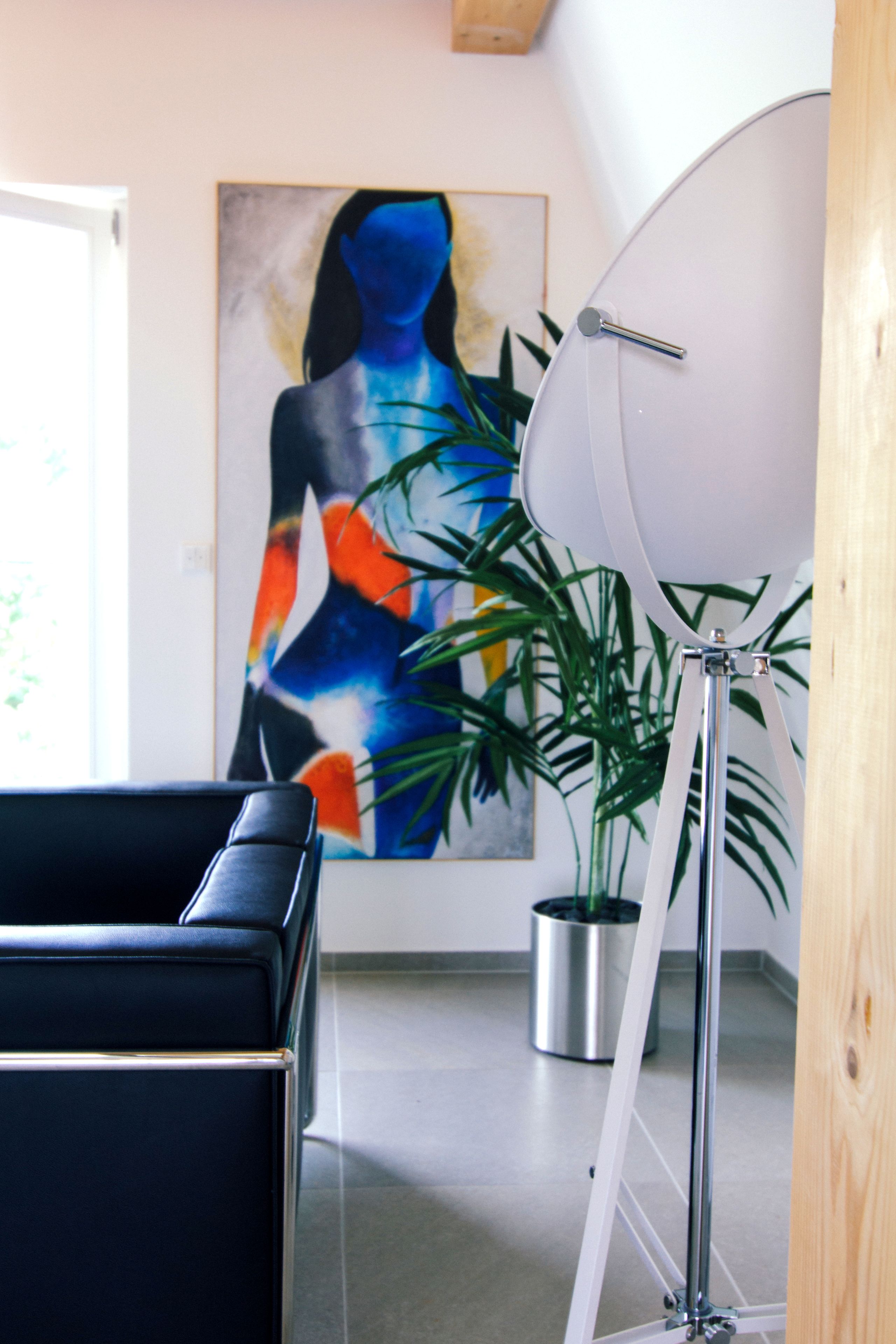 A modern room with a black sofa, a large abstract painting, a potted plant, and a floor lamp.