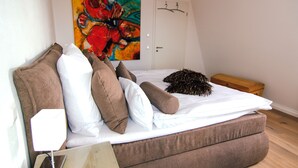 Un dormitorio con cama, almohadas, una mesita de noche, lámpara, un cuadro y un baúl de madera.