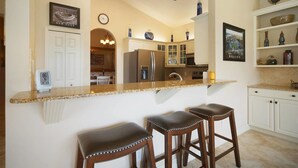 A kitchen with a central island, white cabinetry, and a dining area visible through an archway. - House Bethany by Vacationhit (Cape Coral)
