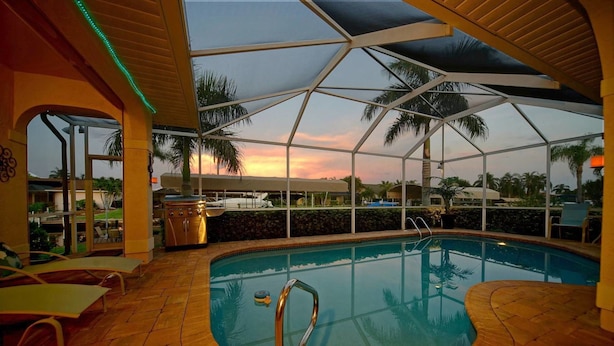 An indoor swimming pool with a view of palm trees and a sunset. - House Bethany by Vacationhit (Cape Coral)