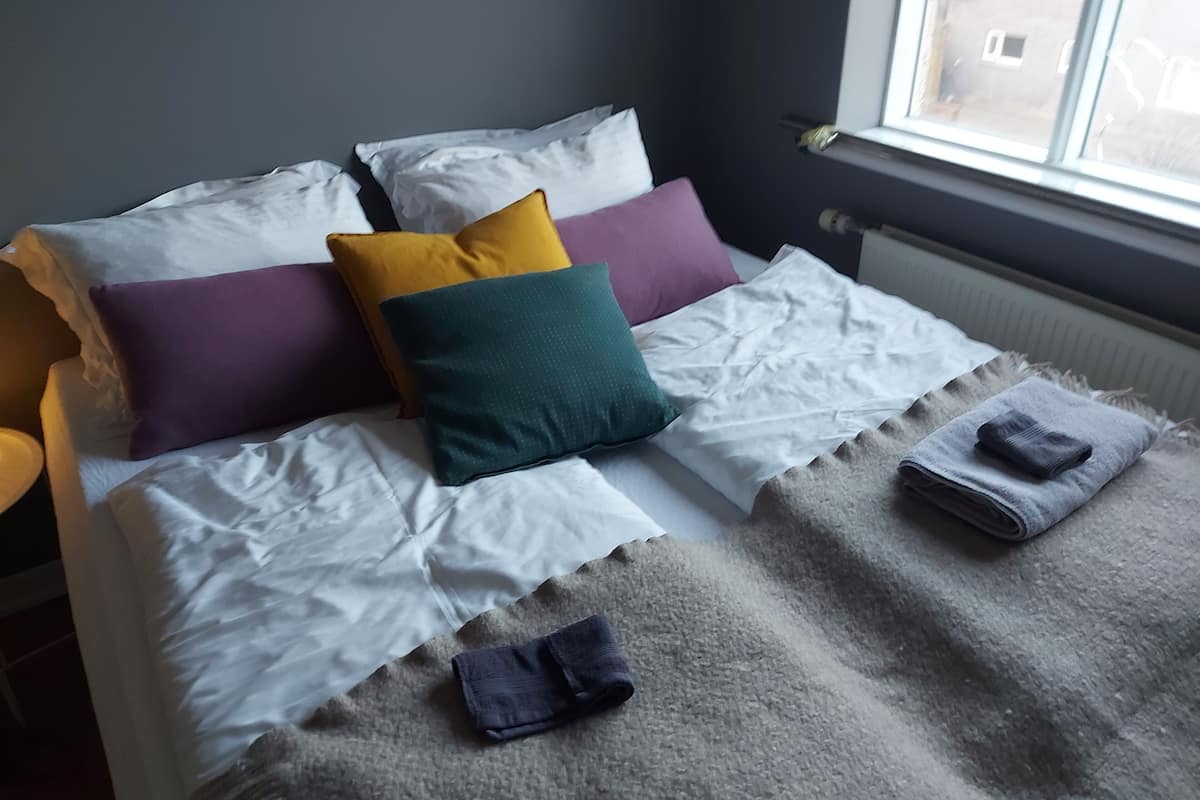 A neatly made bed with white linens and multiple pillows in various colors.