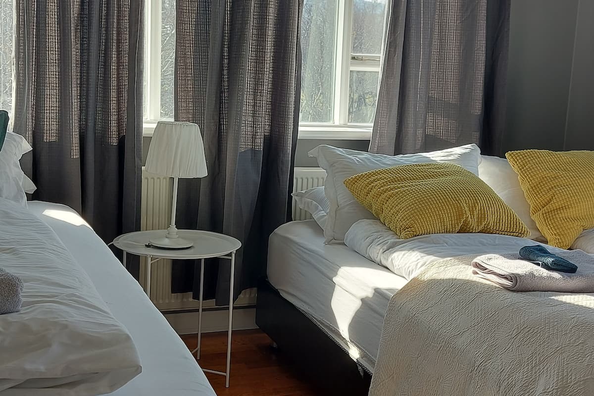 A hotel room with a bed, a bedside table with a lamp, and a window with curtains.