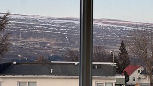 Vista di una catena montuosa innevata attraverso una finestra, con edifici e un lampione visibili in primo piano.