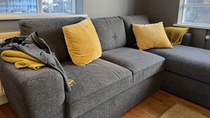 Un divano modulare grigio con due cuscini gialli, una coperta grigia e una coperta gialla su un pavimento in legno.