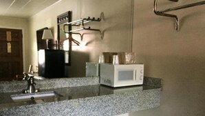 A bathroom with a granite countertop, a white sink, a mirror, a towel rack, and a microwave. - Royal Inn (Monroeville)
