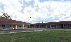 A row of motel buildings with red doors and a parking lot in front.
