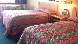 A hotel room with two beds, a small table, and a chair. There is a window with curtains, a painting on the wall, and a lamp on the nightstand. - Royal Inn (Monroeville)