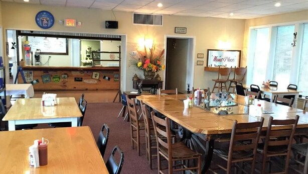 A restaurant with wooden tables and chairs, a counter, and a clock on the wall. - Royal Inn (Monroeville)