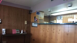 A reception area with a wooden wall, a reception desk, a telephone, and a bulletin board. - Royal Inn (Monroeville)