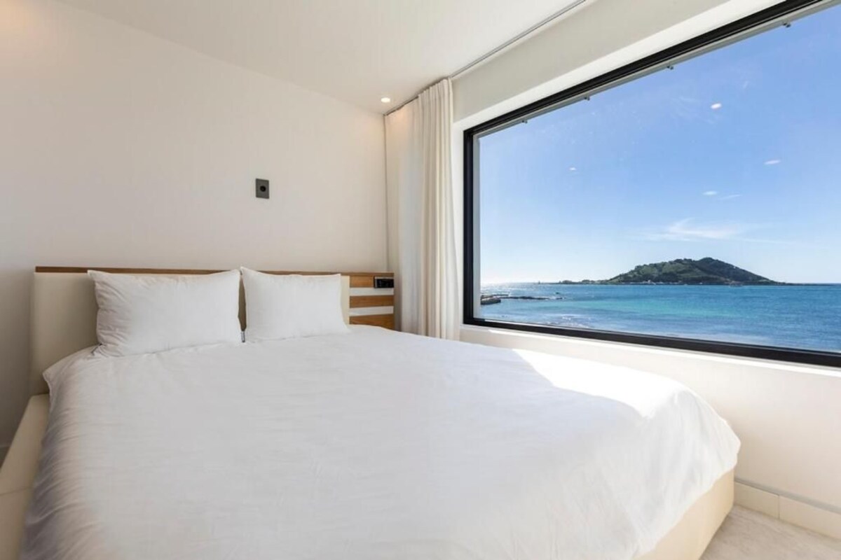 Ein Schlafzimmer mit einem großen Bett, einem Fenster mit Meerblick und einem schlichten, modernen Design.