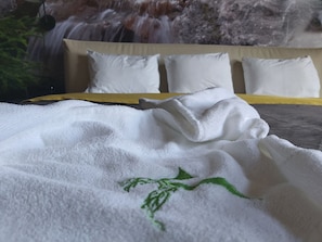 A bed with white pillows and a white towel with green embroidery.