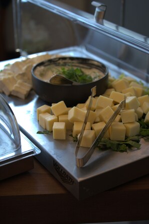 A buffet with cubed cheese, a dipping sauce, and a bowl of greens.