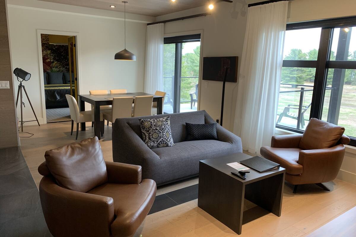 Un salon moderne avec un canapé gris, deux fauteuils en cuir marron, une table basse et un coin repas comprenant une table et des chaises.