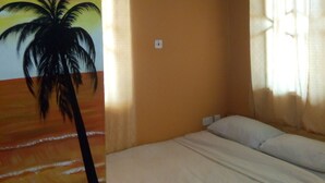 A room with a bed, an air conditioner, a wall with a palm tree painting, and a window with curtains. - Feehi's Place - Hostel (Accra)