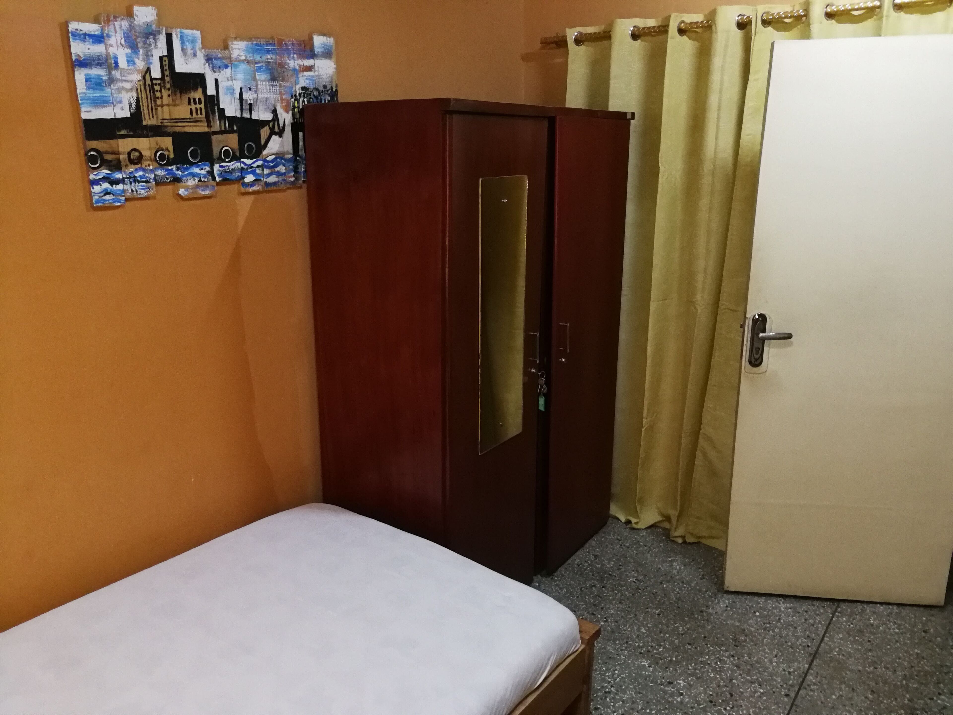 A room with a bed, a wardrobe, a door, and a wall with a poster.