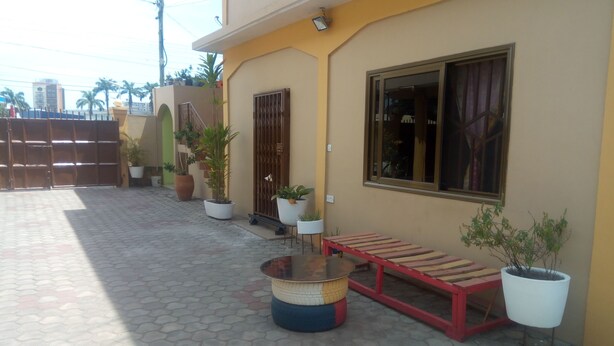 A courtyard with a tiled floor, a bench, potted plants, and a gate. - Feehi's Place - Hostel (Accra)