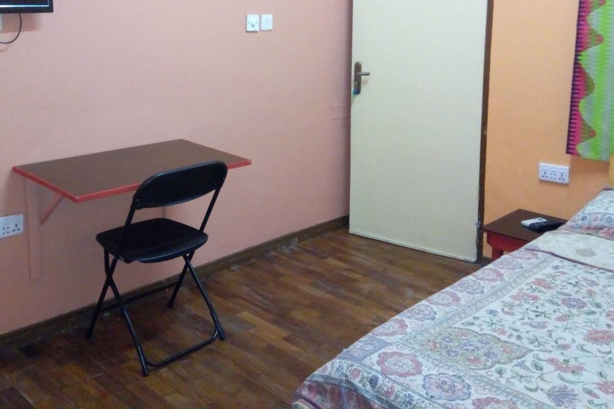 Ein kleines Zimmer mit Schreibtisch, Stuhl, Bett und einer Tür.