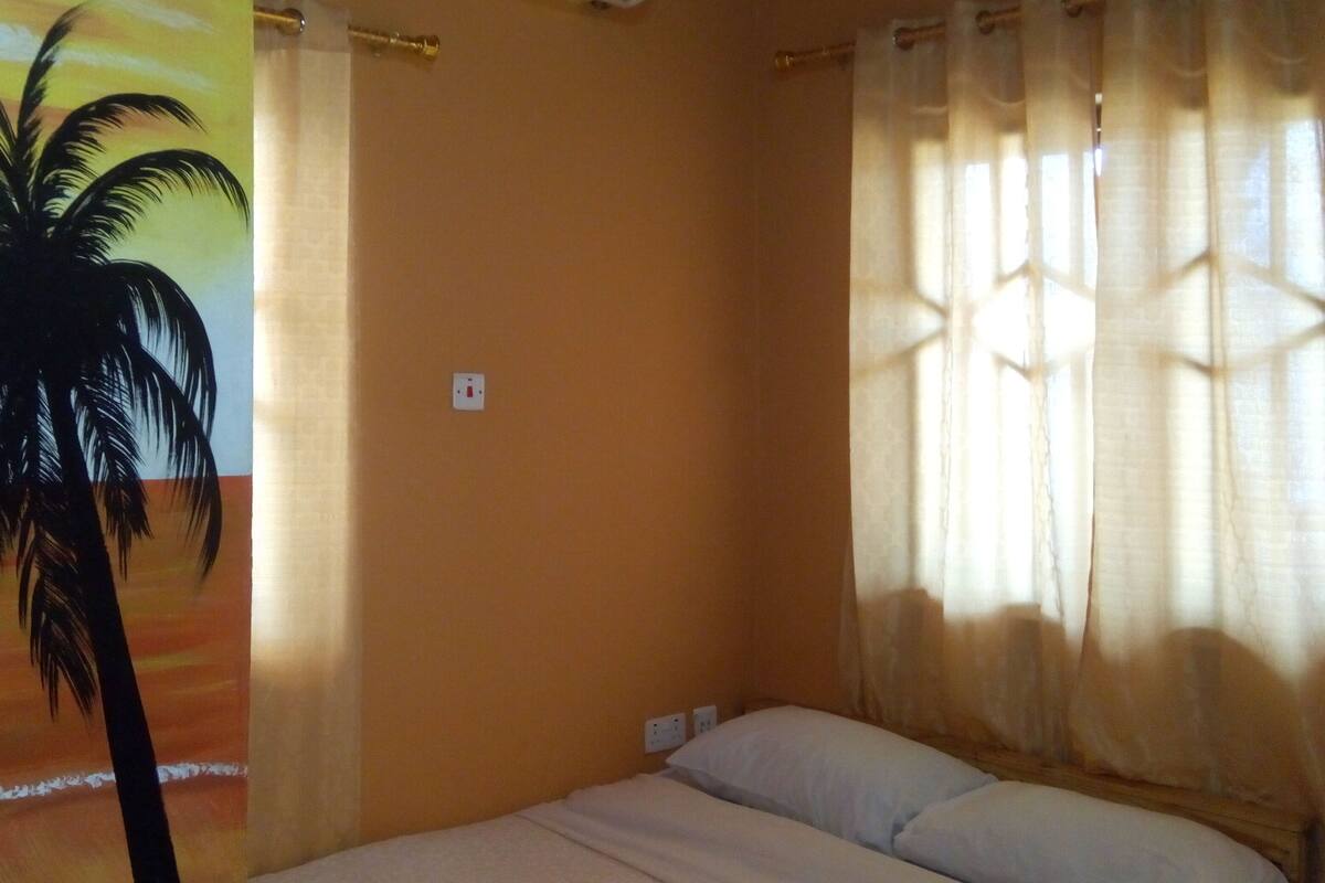 Ein Zimmer mit einem Bett, einer Klimaanlage, einer Wand mit Steckdose und einem Fenster mit Vorhängen.