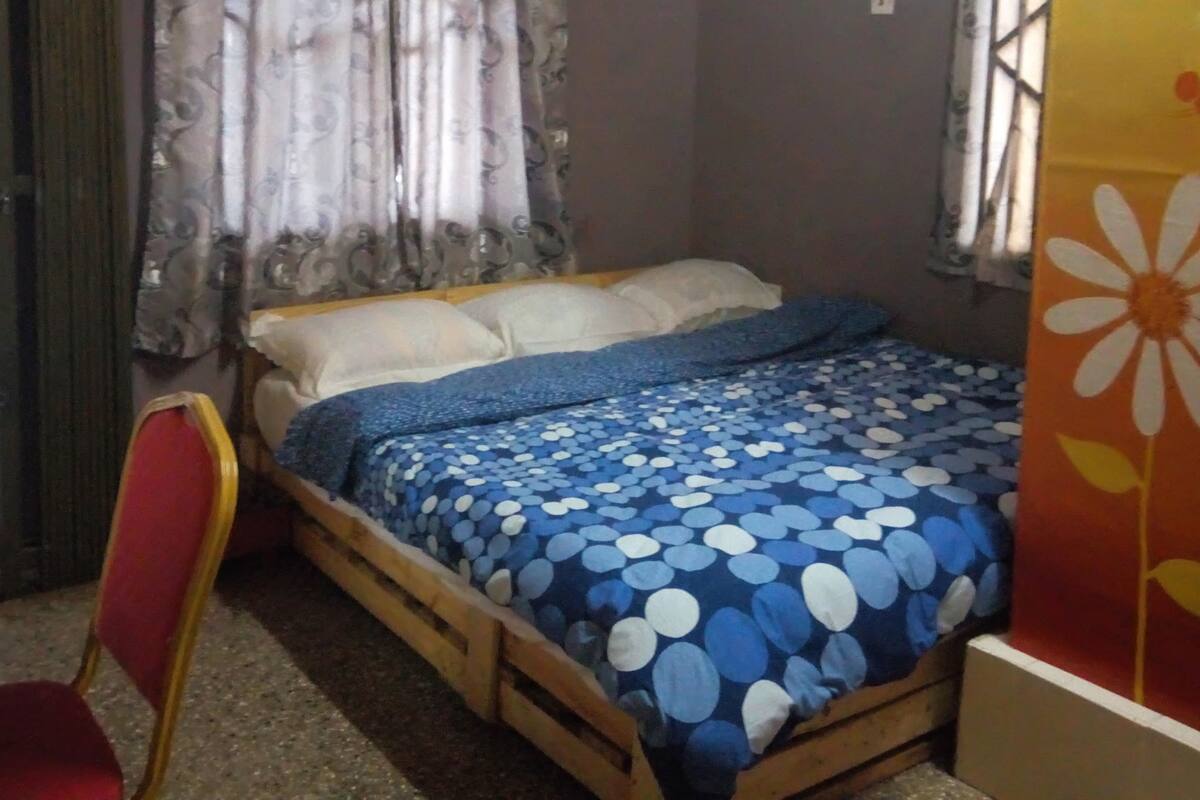 Ein Schlafzimmer mit einem Bett, einem Sessel, Vorhängen und einer Klimaanlage.
