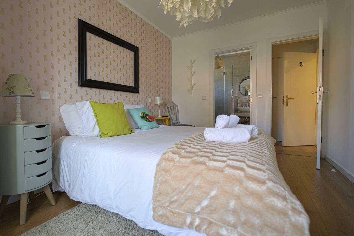 A neatly arranged bedroom with a bed, bedside tables, and a door leading to a bathroom.