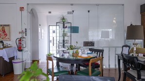 A dining area with a round glass table, chairs, and a small plant. There is a fire extinguisher on the wall and a trash bin near the entrance. - Casa das Hortênsias - Charming Guest House (Sintra)