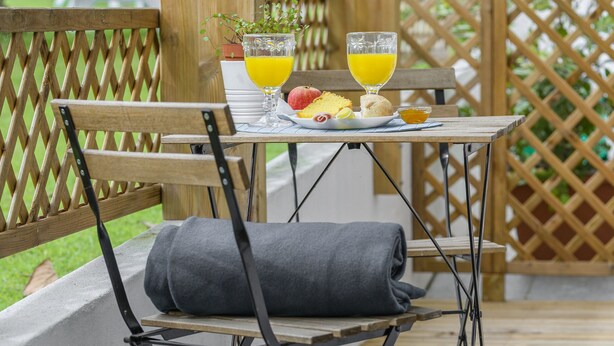 A wooden deck with a table and chairs, a small potted plant, and a glass of orange juice. - Casa das Hortênsias - Charming Guest House (Sintra)