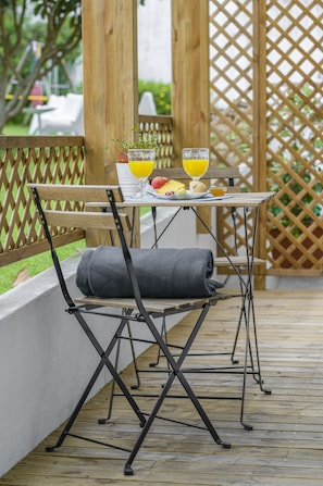 A wooden deck with a table and chairs, a small potted plant, and a glass of orange juice. - Casa das Hortênsias - Charming Guest House (Sintra)