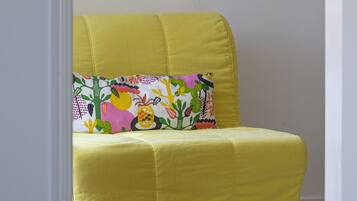 Un sillón amarillo con un cojín floral de colores, ubicado en una habitación con una fotografía en blanco y negro enmarcada en la pared.