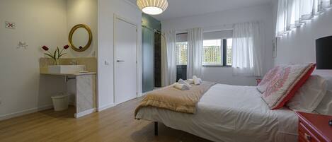Una camera da letto con un letto, un comodino, una finestra con tende e un bagno con lavandino e specchio.