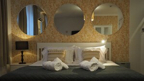 A neatly made bed with two rolled towels, a bedside lamp, and three wall mirrors. - Casa das Hortênsias - Charming Guest House (Sintra)