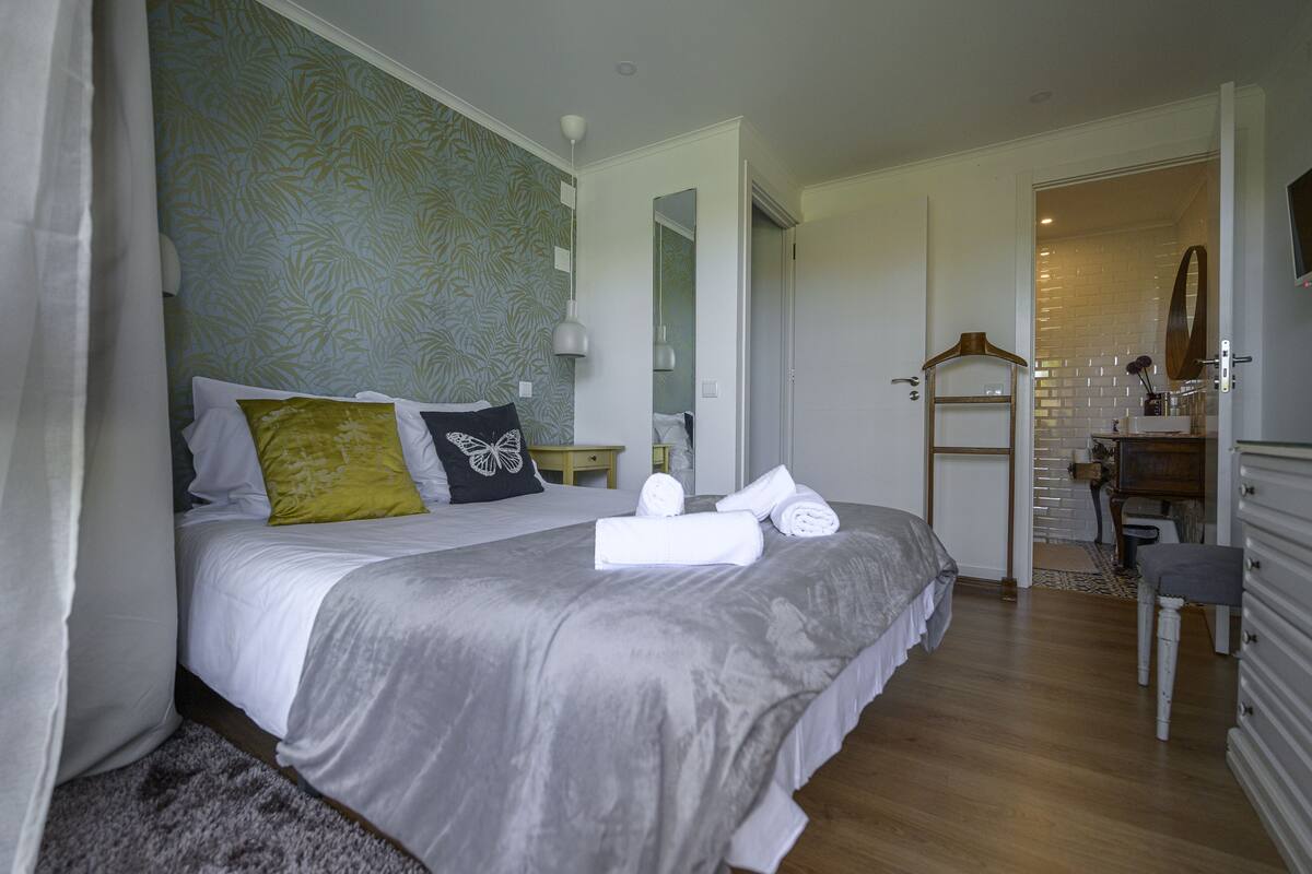 A neatly made bed with pillows, a bedside table, and a mirror.