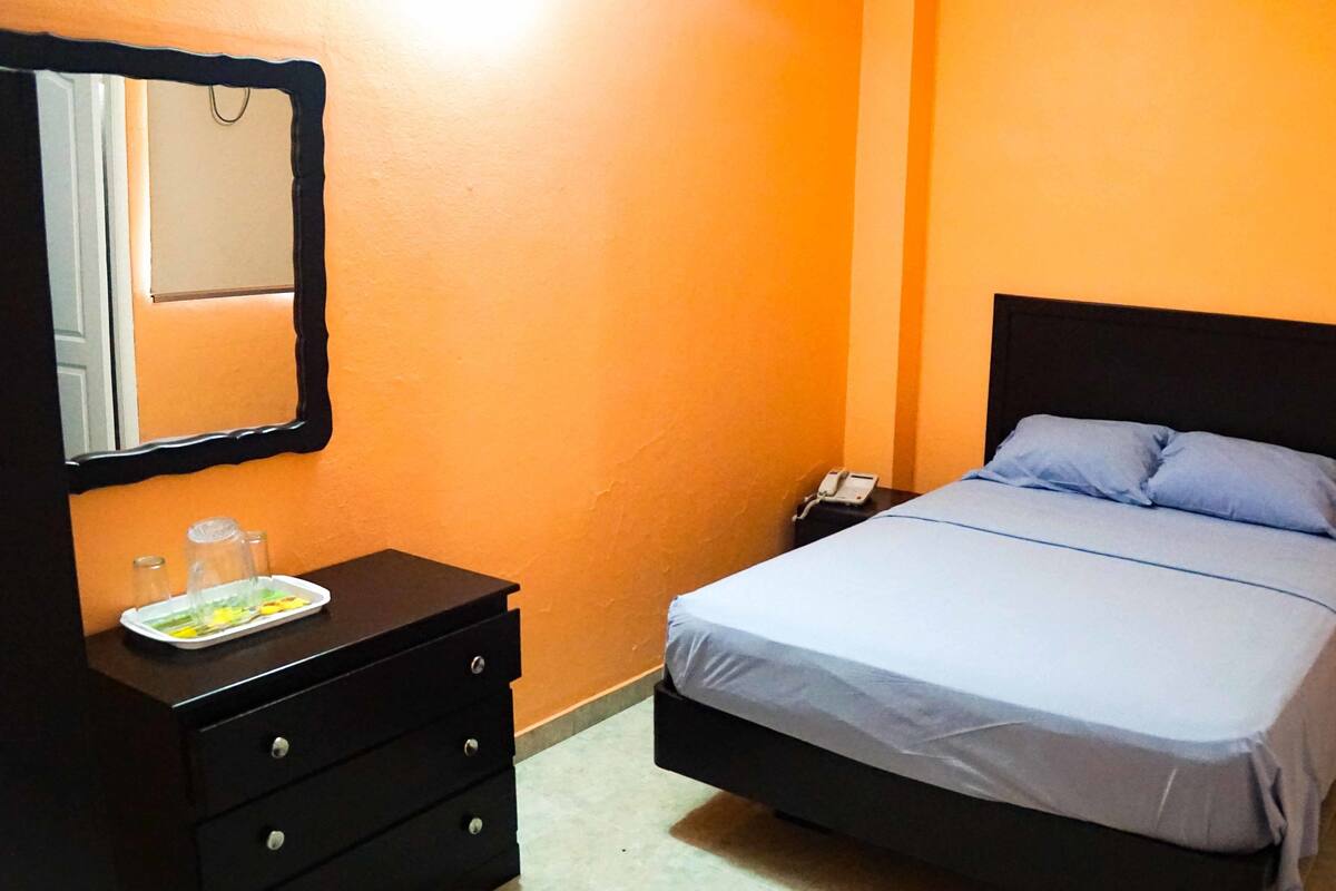 Een slaapkamer met een bed, een dressoir, een nachtkastje, een spiegel en een telefoon.