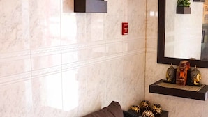 Una sala de estar moderna con un sofá marrón oscuro, paredes de mármol y plantas decorativas.