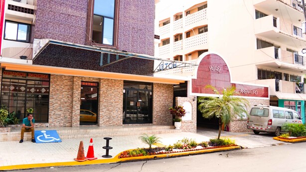 Un hotel con un arco rojo en la entrada, un cartel que dice 'HABITACIONES ECONOMICAS' y un letrero de estacionamiento para discapacitados.