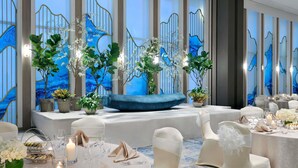 Un salón de banquetes con mesas redondas, sillas blancas y un banco acolchado azul.