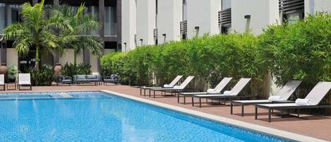 Una piscina con sillones de descanso, rodeada de follaje y edificios modernos.