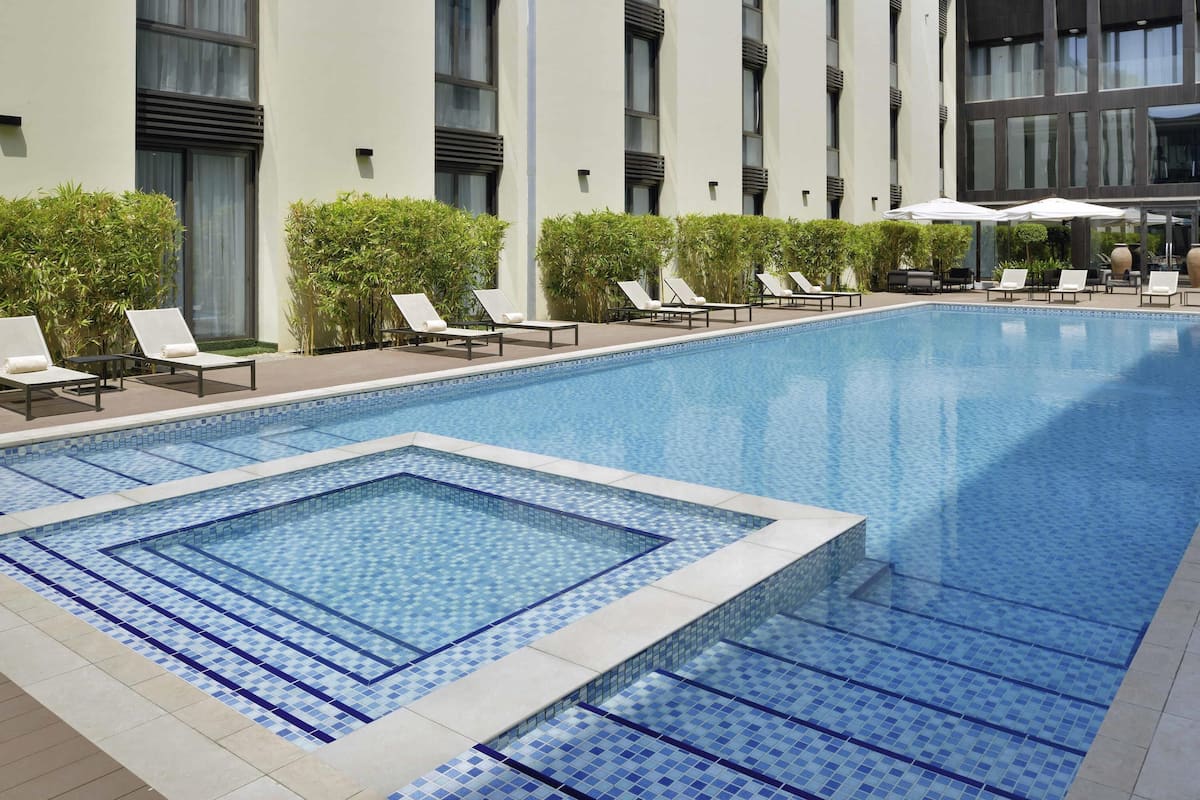 Zona de piscina moderna de hotel con sillones de descanso y una piscina con mosaicos.
