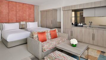 A modern hotel room with two beds, a sofa, a small table, and a kitchenette.
