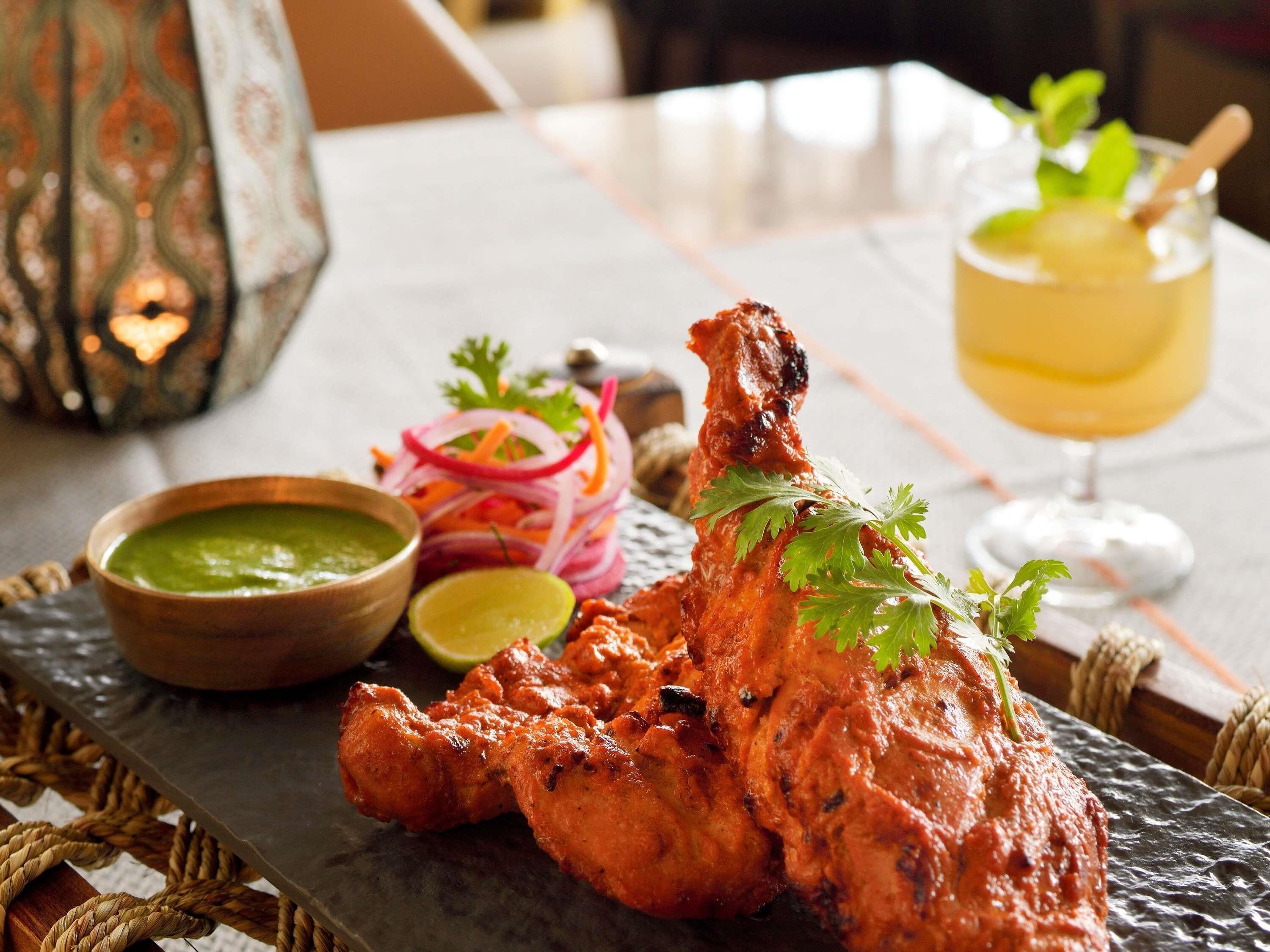 A table with a roasted chicken leg, a glass of drink, and a bowl of sauce.