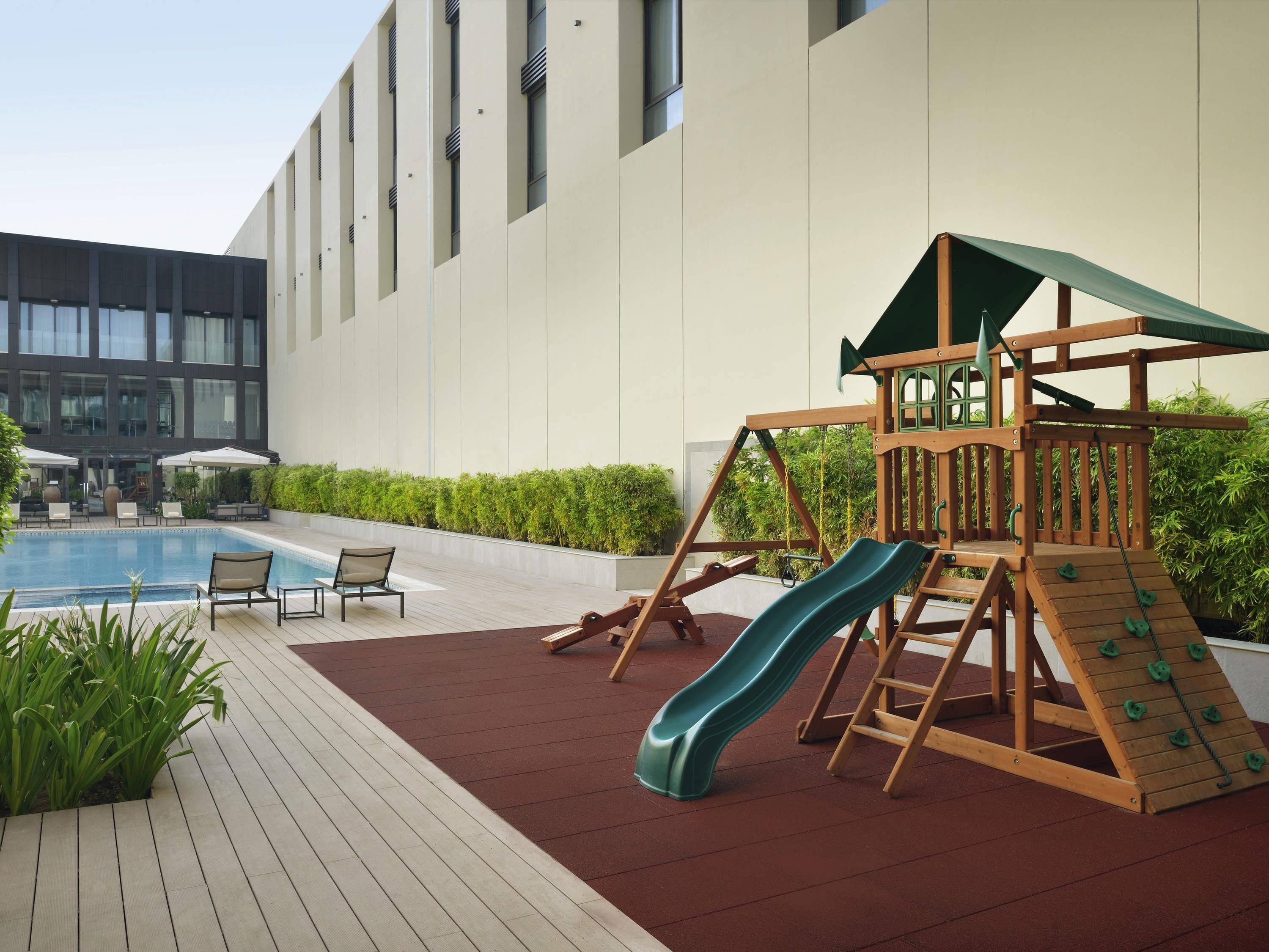 A children's play area with a slide and climbing structure, a pool, and lounge chairs.