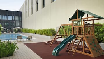 A children's play area with a slide and climbing structure, a pool, and lounge chairs.