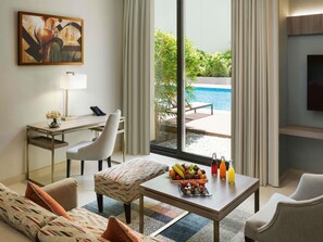 A hotel room with a desk, a sofa, a coffee table with fruit and drinks, a TV, and a view of a pool. - Mövenpick Hotel Tahlia Jeddah (Jeddah)