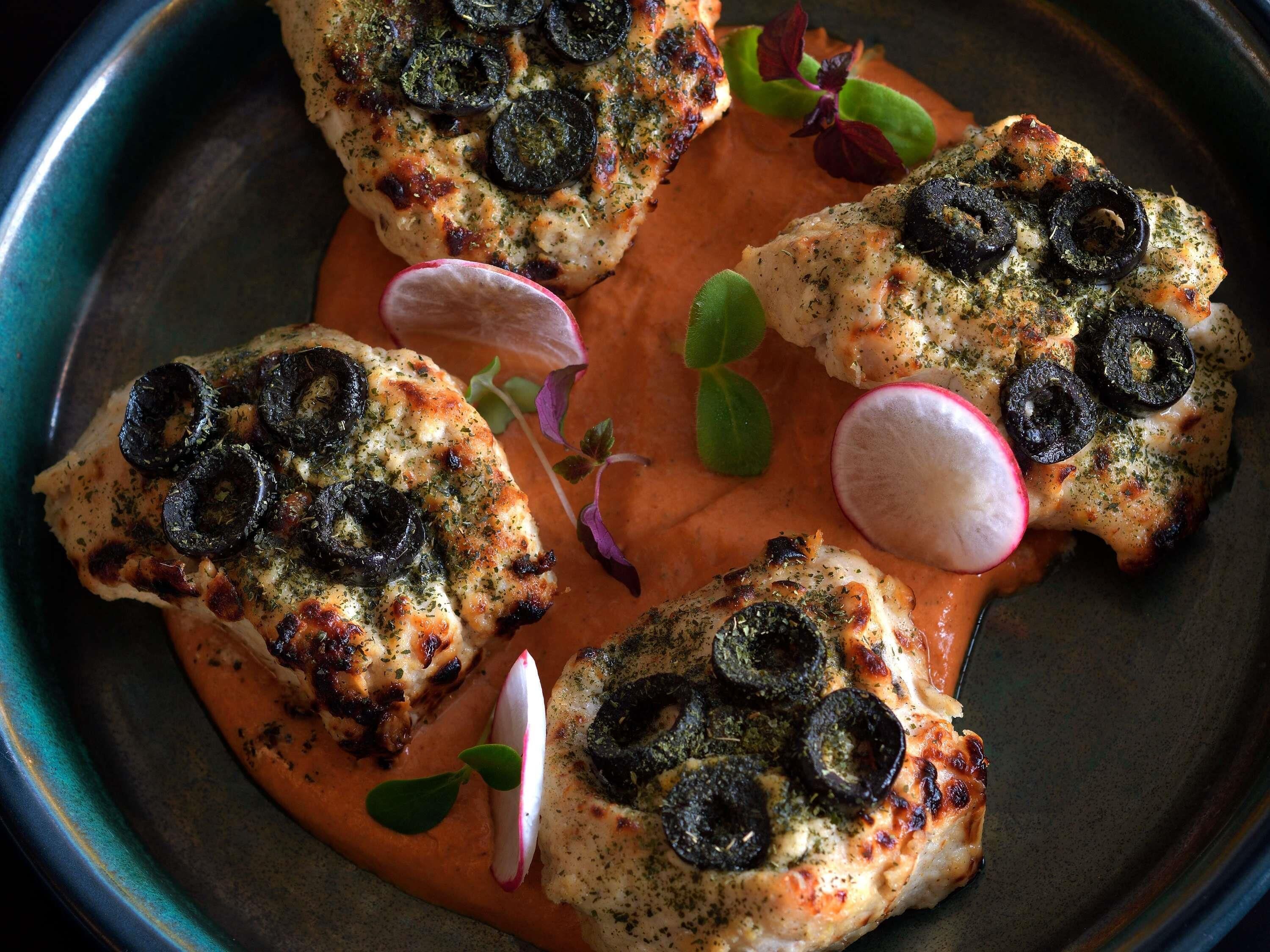 A dish with grilled chicken, black olives, and herbs.