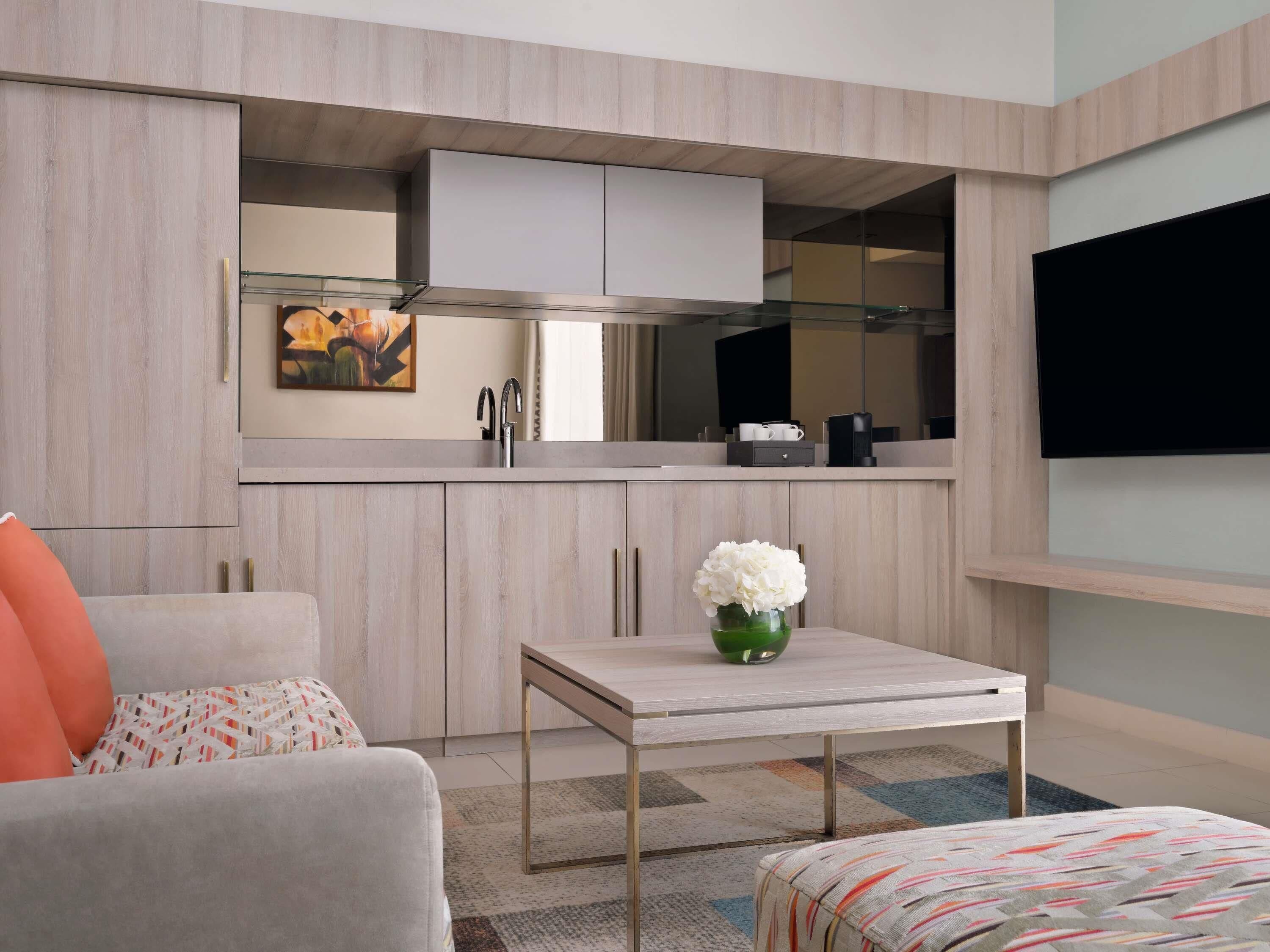 A compact living space with a kitchenette, a sofa, a coffee table, and a flat-screen TV mounted on the wall.