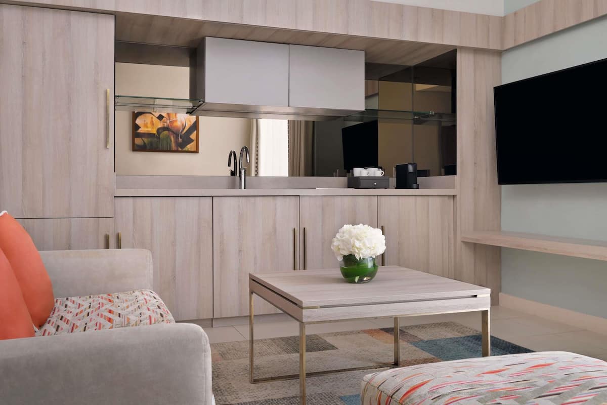 A compact living space with a kitchenette, a sofa, a coffee table, and a flat-screen TV mounted on the wall.