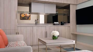 A compact living space with a kitchenette, a sofa, a coffee table, and a flat-screen TV mounted on the wall.