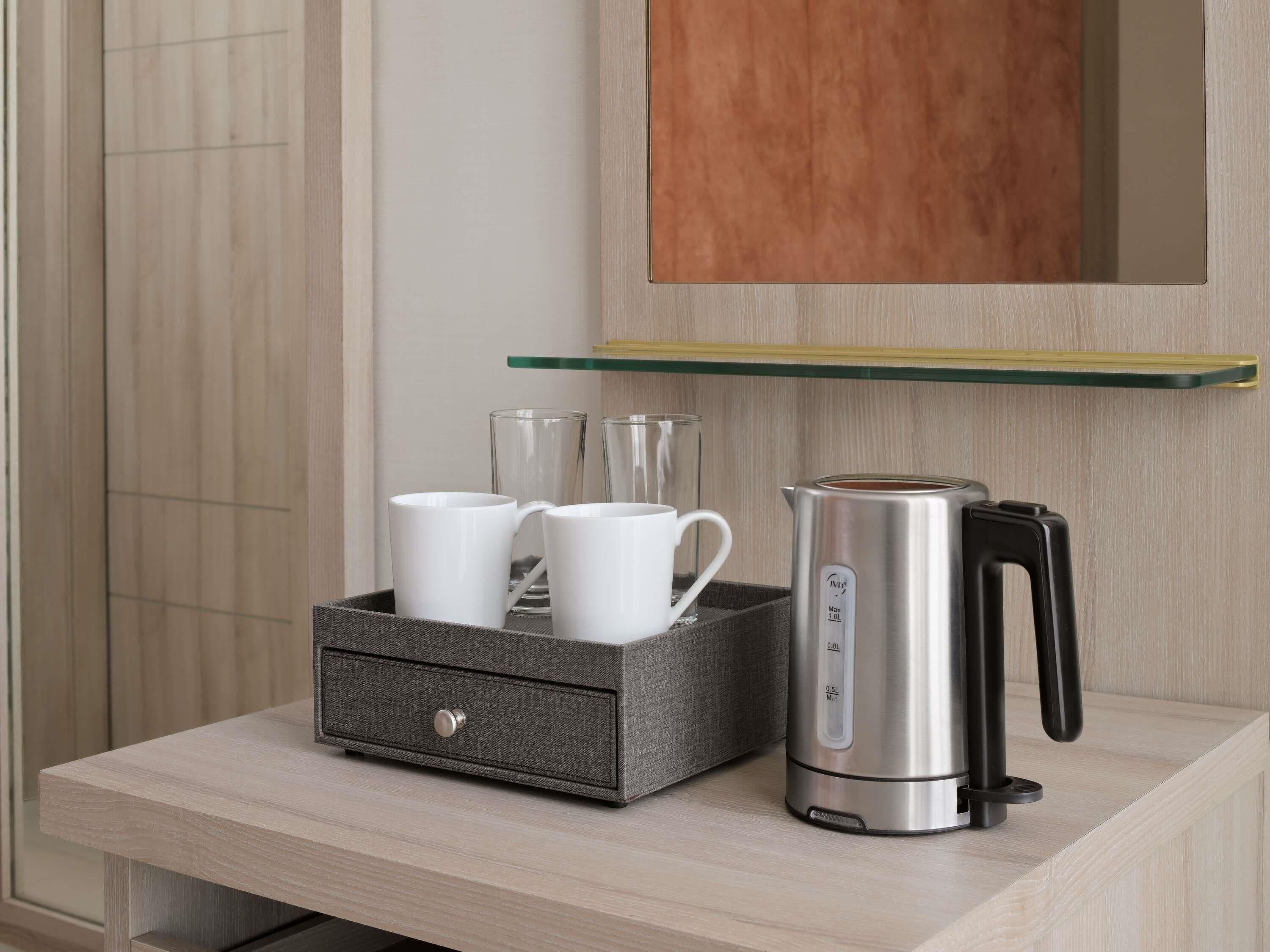 A coffee maker and a mug holder on a wooden counter with a mirror above.