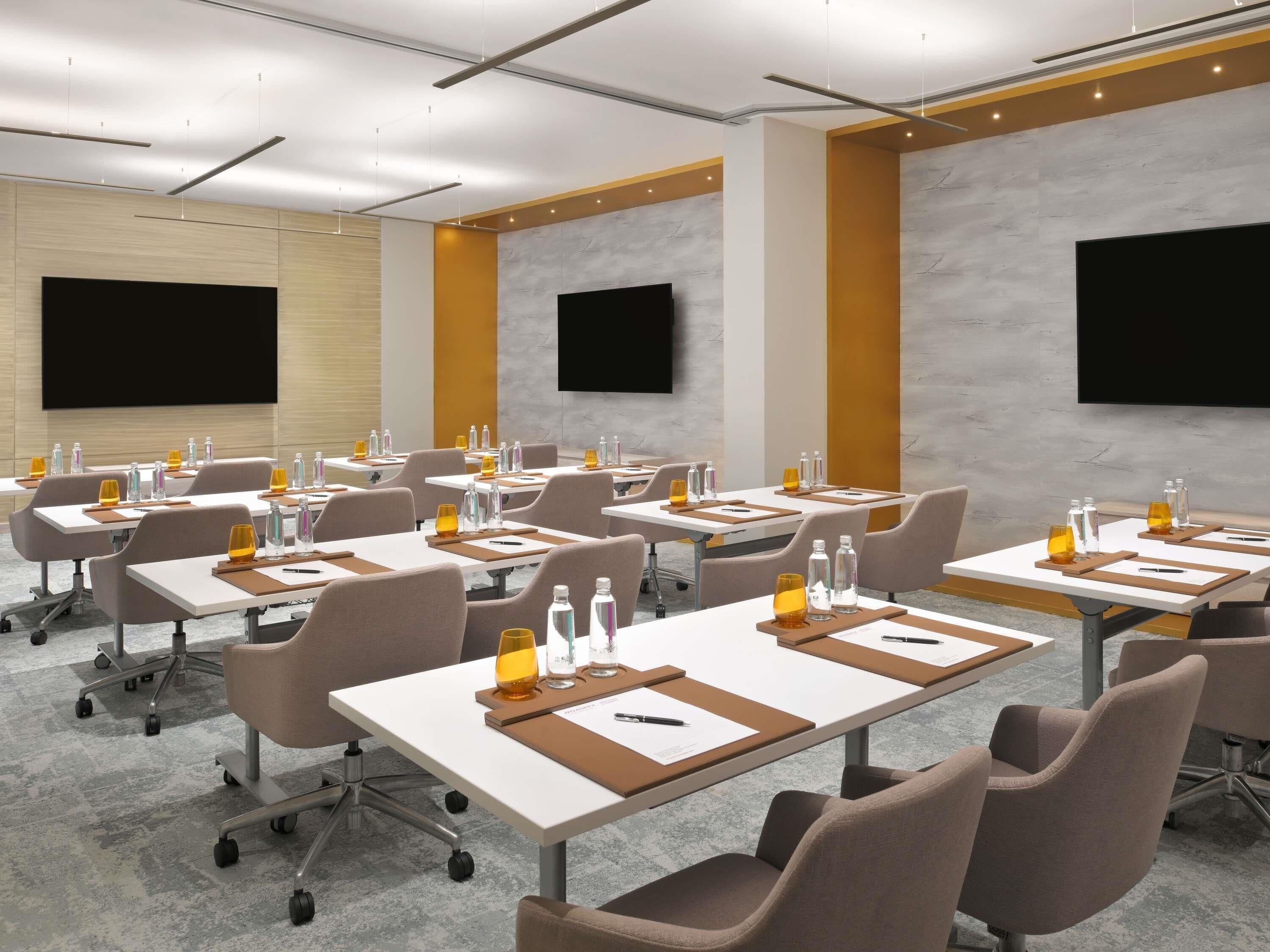 A conference room with tables, chairs, and a large screen.