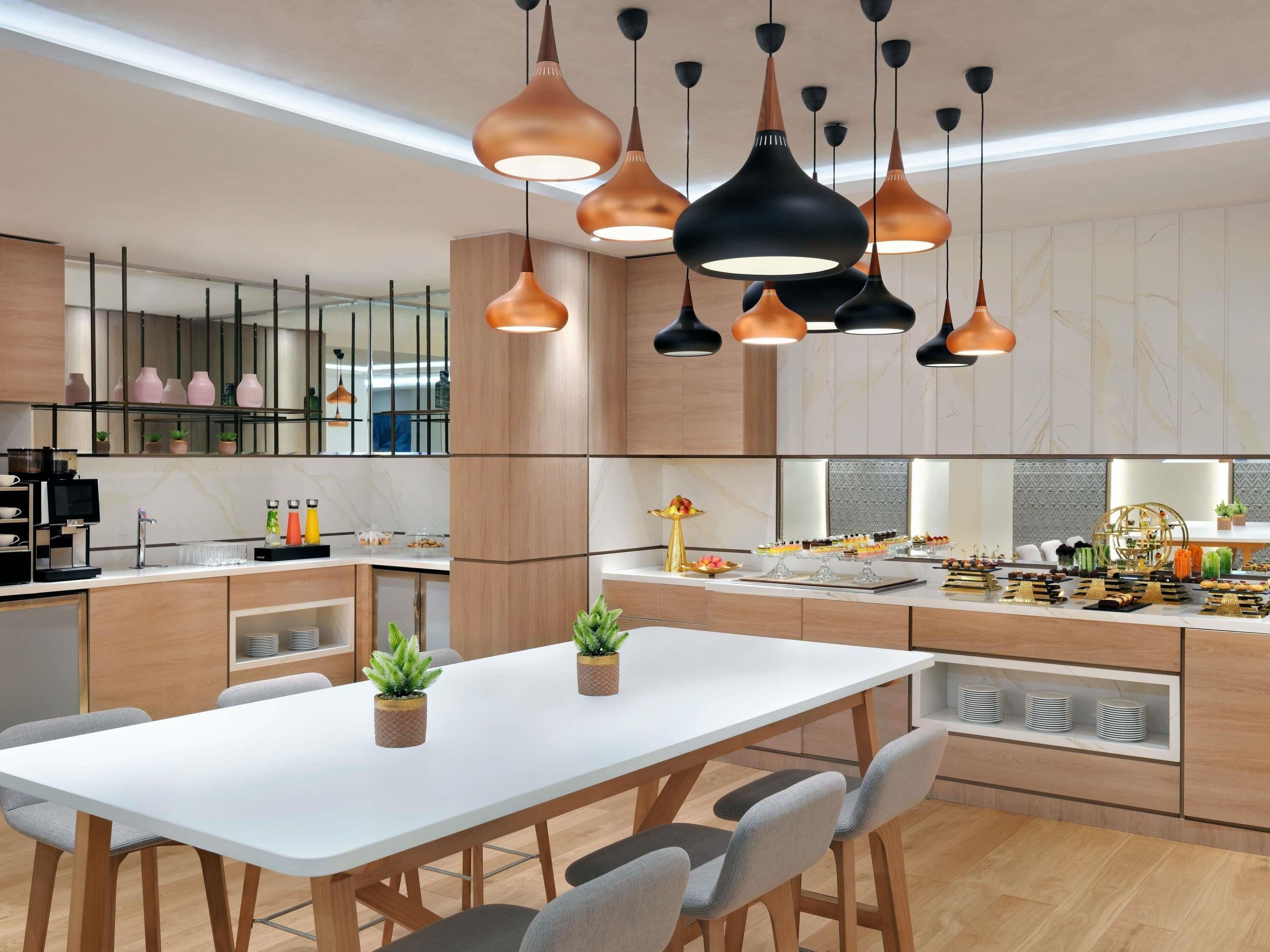 Cozinha moderna com iluminação pendente, uma mesa de jantar branca e diversos eletrodomésticos e objetos de decoração.